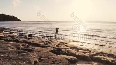 无人驾驶飞机俯瞰年轻有思想的女人戴着帽子站在海滩上观看海景。